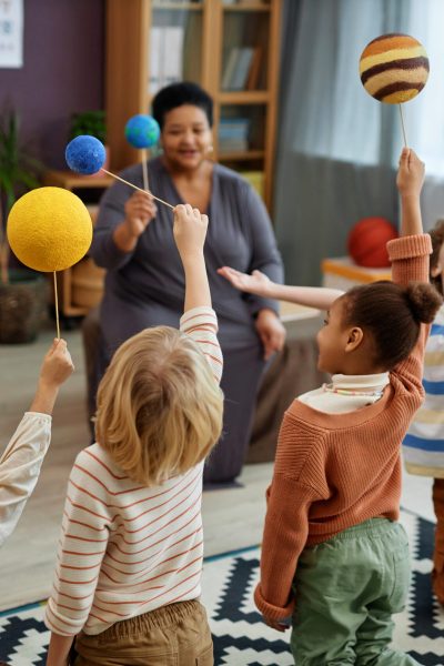 Diverse group of kids playing with planet models enjoying class in preschool