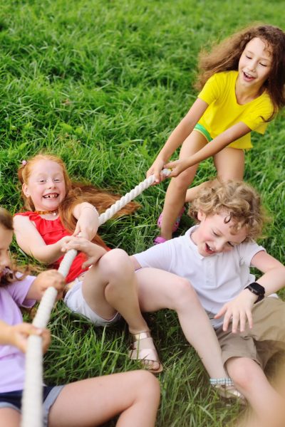 group of preschool children - boys and girls compete in a tug of war against the background of a park and greenery.