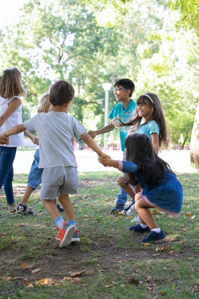 Happy children playing together outdoors, dancing around on grass, enjoying outdoor activities and having fun in park. Kids party or friendship concept