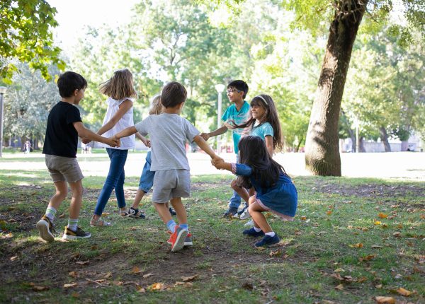 Happy children playing together outdoors, dancing around on grass, enjoying outdoor activities and having fun in park. Kids party or friendship concept